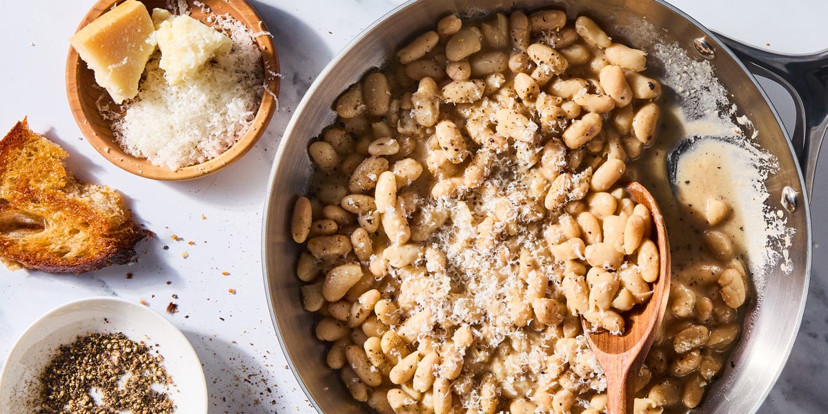 cacio e pepe white beans skillet with a wooden spoon beside a plate of cheese