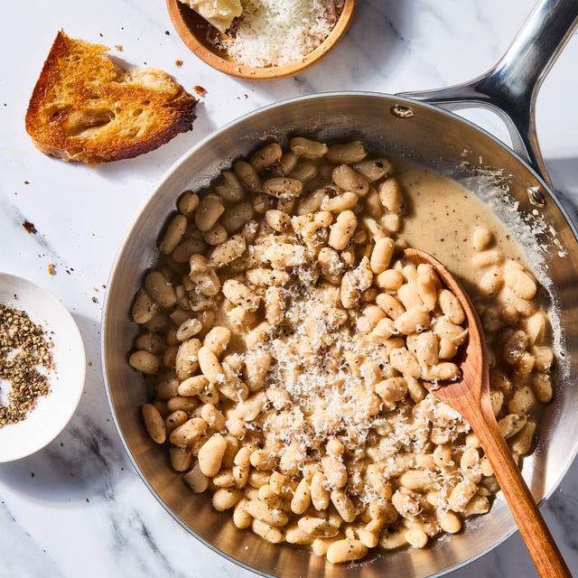 cacio e pepe white beans skillet with a wooden spoon beside a bowl of cheese