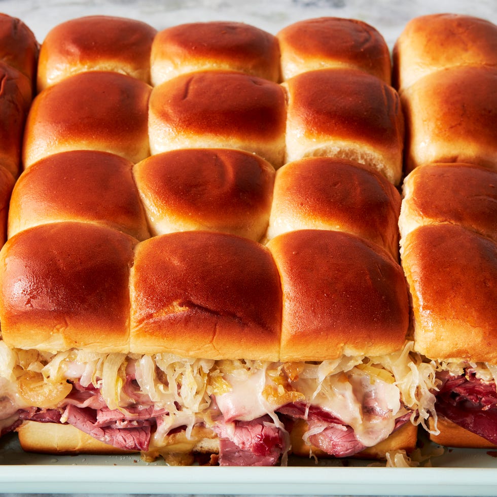 a tray of sliders made with hawaiian rolls, corned beef, sauerkraut, and swiss cheese