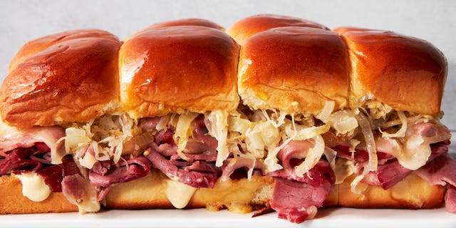 a tray of sliders made with hawaiian rolls, corned beef, sauerkraut, and swiss cheese