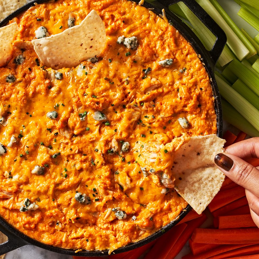 buffalo chicken dip in a skillet with celery and carrots beside and a tortilla chip dipping in