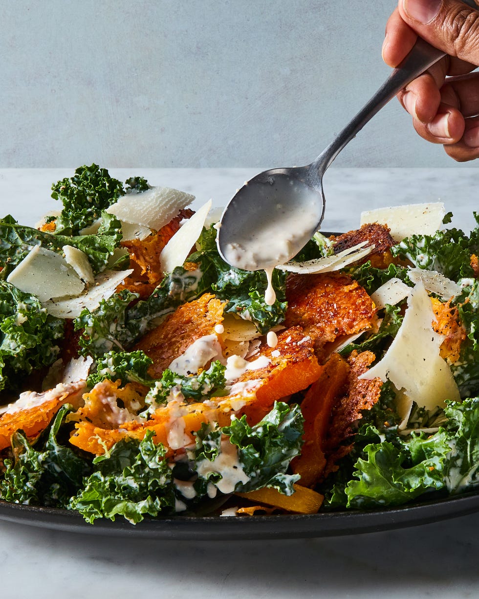 harvest caesar salad with squash croutons, parmesan, and caesar dressing drizzling over from a spoon