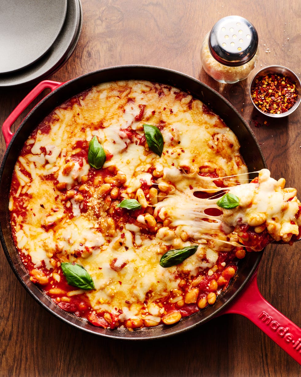 pizza beans skillet topped with mozzarella, parmesan, and basil, with a spoon coming out