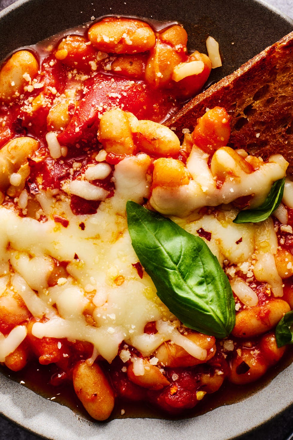 Pizza beans skillet pizza beans topped with mozzarella and parmesan and basil in a bowl with a piece of toast