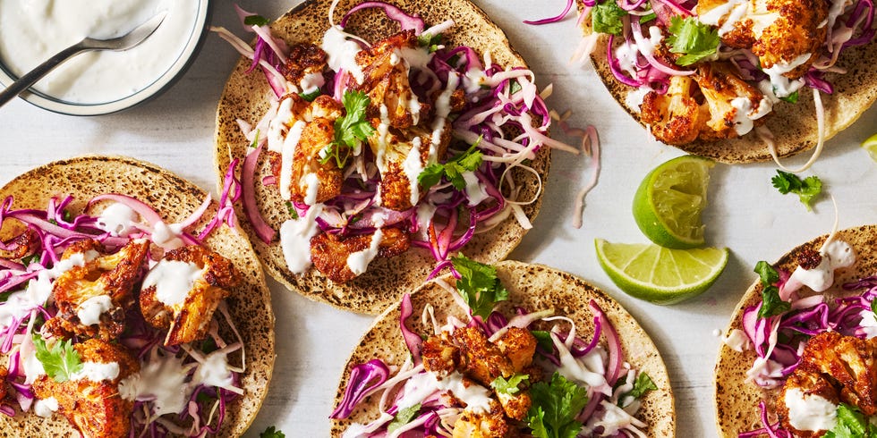 cauliflower tacos topped with cabbage, cilantro, and sour cream sauce beside a bowl of sour cream sauce