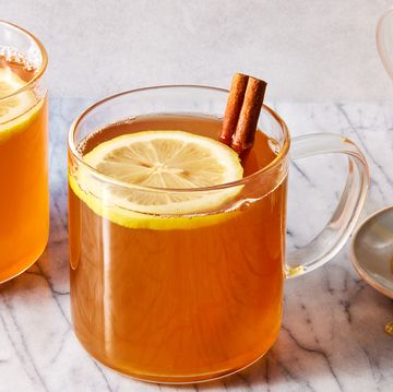 a glass mug filled with warm whiskey, honey, and water garnished with lemon slices and cinnamon sticks