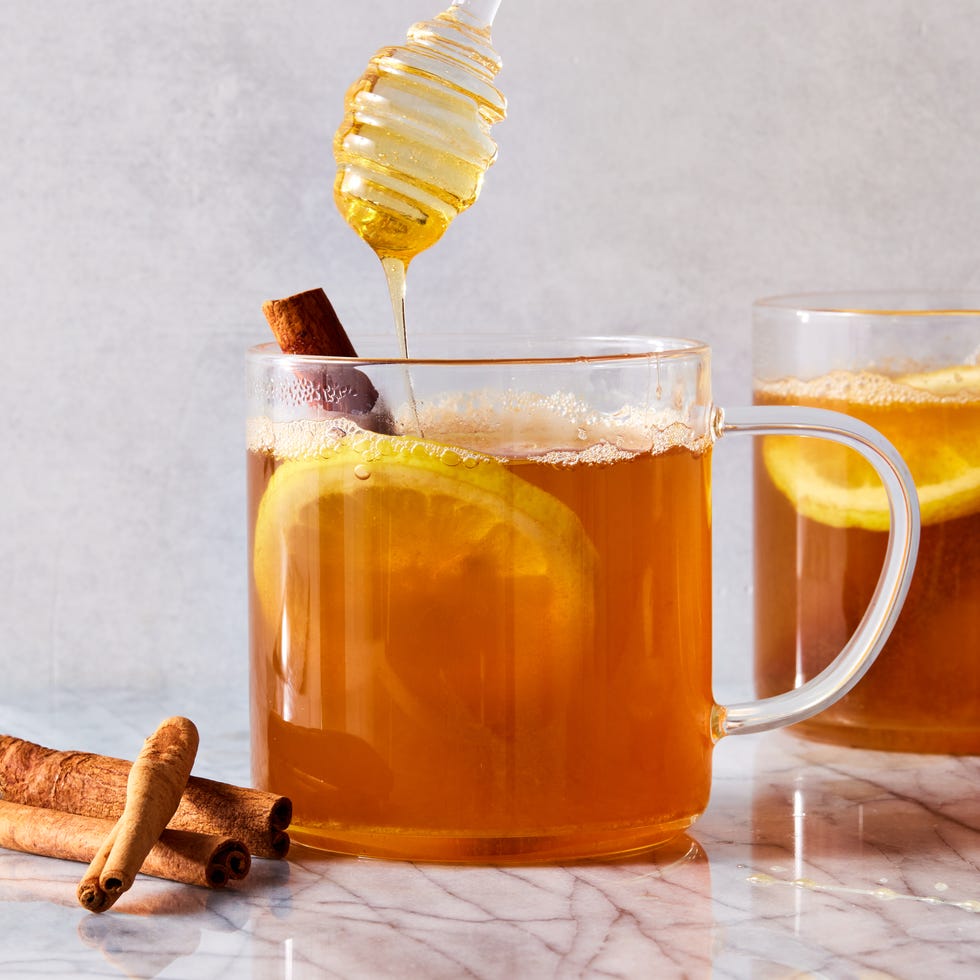 a glass mug filled with warm whiskey, honey, and water garnished with lemon slices and cinnamon sticks