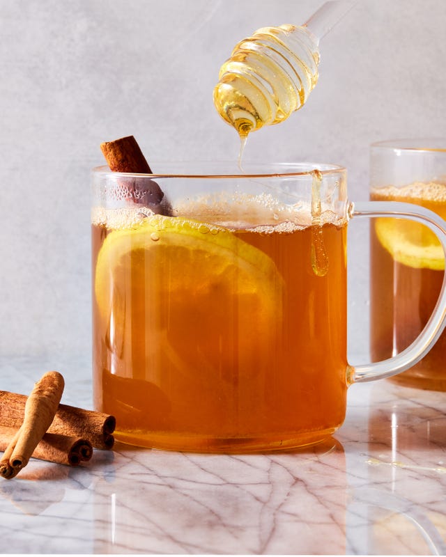 a glass mug filled with warm whiskey, honey, and water garnished with lemon slices and cinnamon sticks