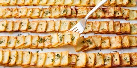 crispy domino potatoes in rows topped with thyme and flaky salt with a fork lifting one