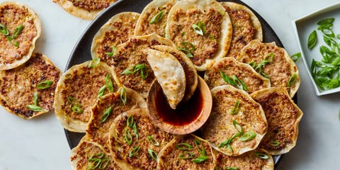 plate of smash dumplings topped with sliced scallions with a bowl of soy sauce in the middle
