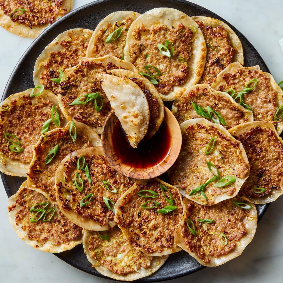 plate of smash dumplings topped with scallions with a bowl of soy sauce in the middle