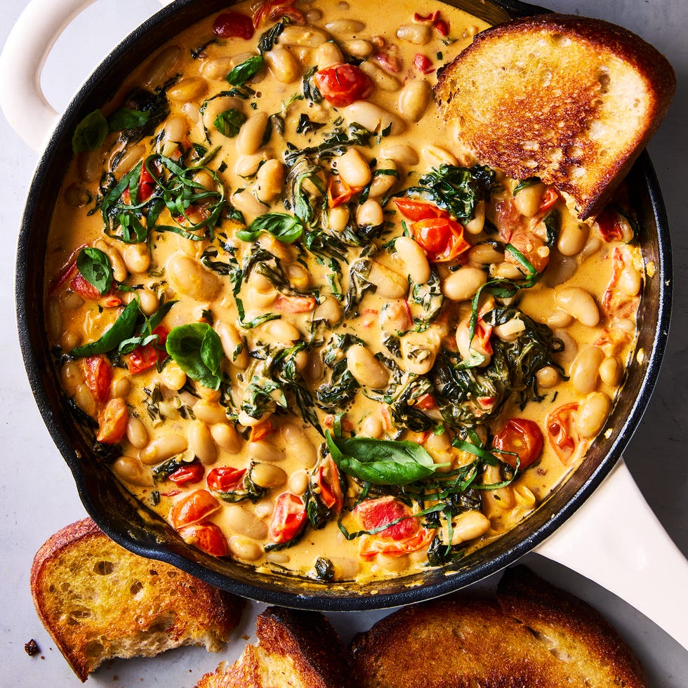 cast iron skillet filled with creamy tuscan white beans topped with basil, with toast alongside