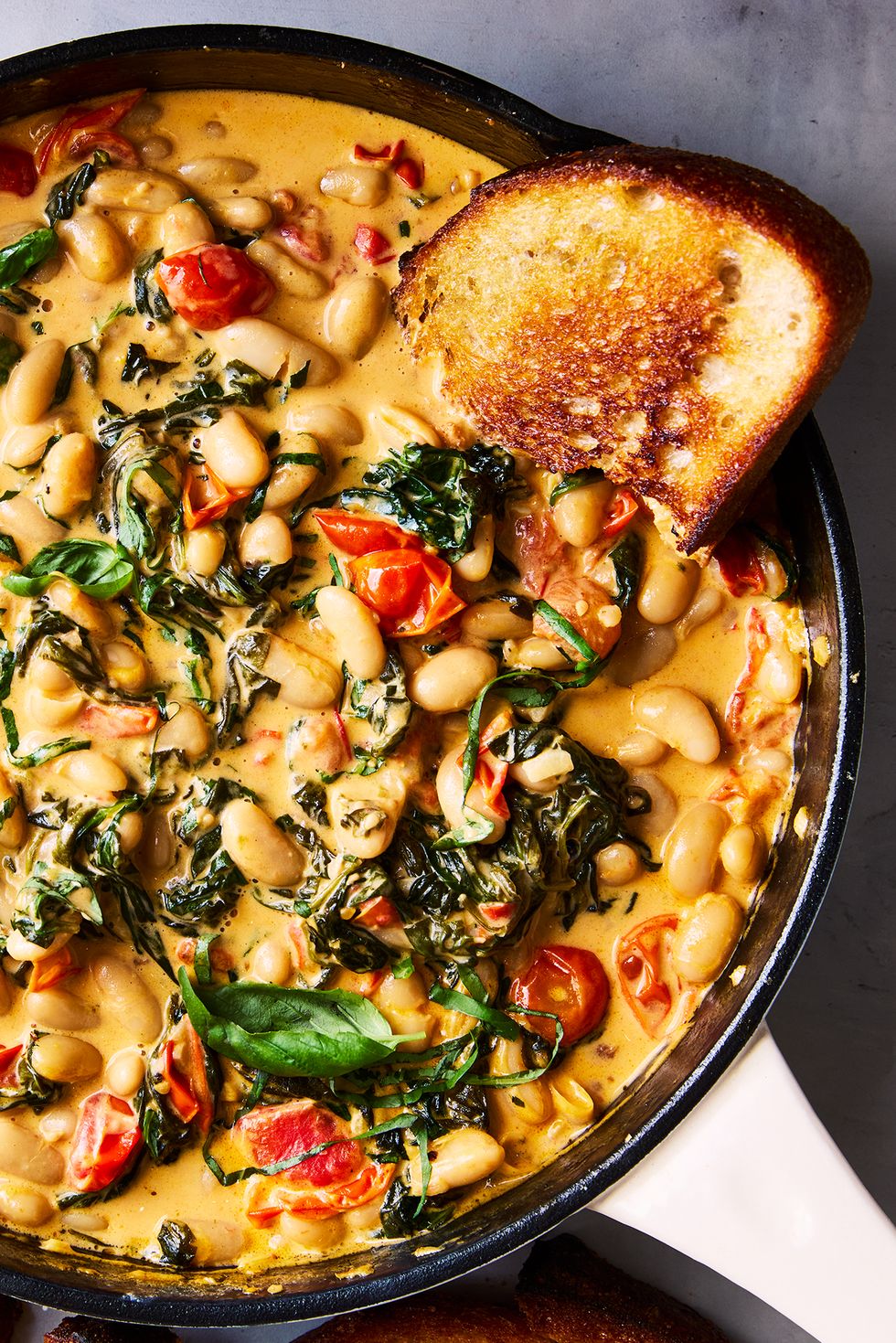 cast iron skillet filled with creamy tuscan white beans topped with basil, with toast alongside