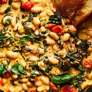cast iron skillet filled with creamy tuscan white beans topped with basil, with toast alongside
