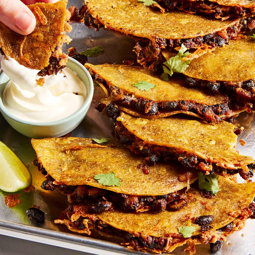 crispy sheet pan black bean tacos on a sheet pan with one dipped into a bowl of sour cream