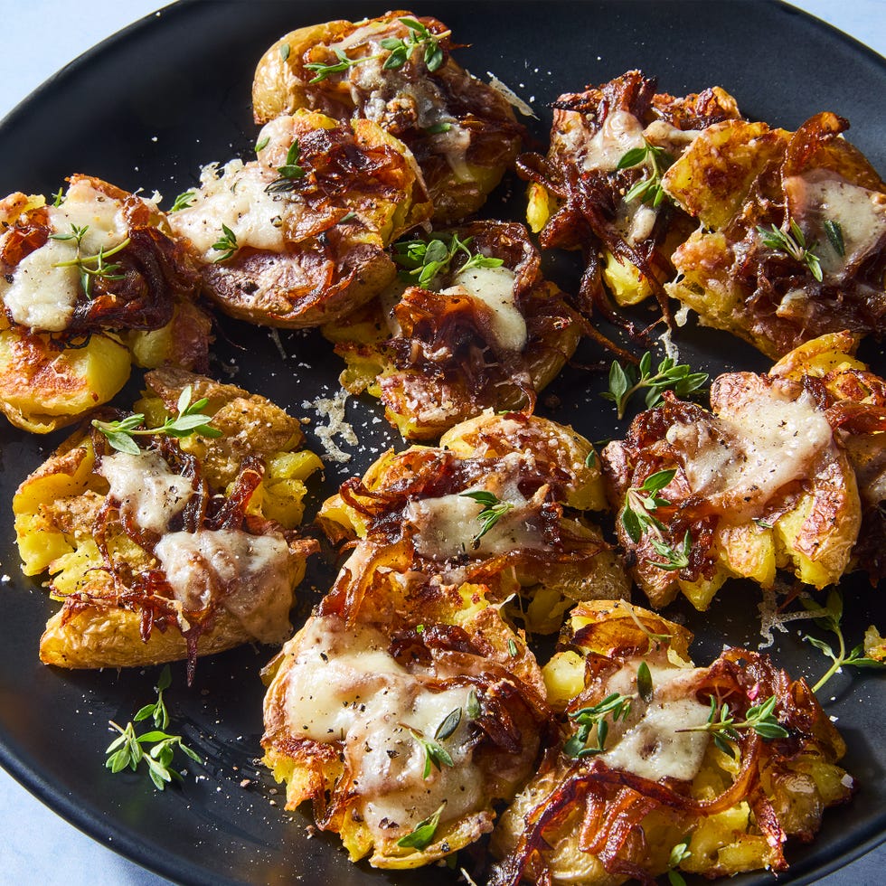 french onion smashed potatoes topped with caramelized onions, gruyere, and thyme on a plate