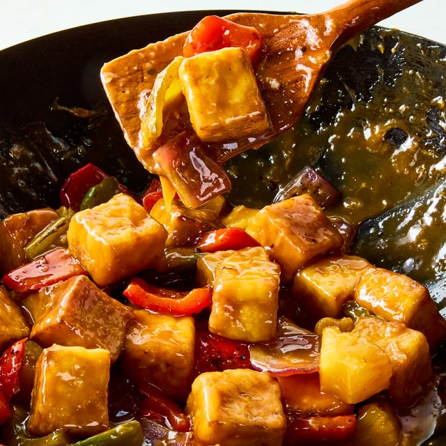 a pan of crispy tofu cubes with red onion, bell peppers, pineapple, and a sweet and sour sauce