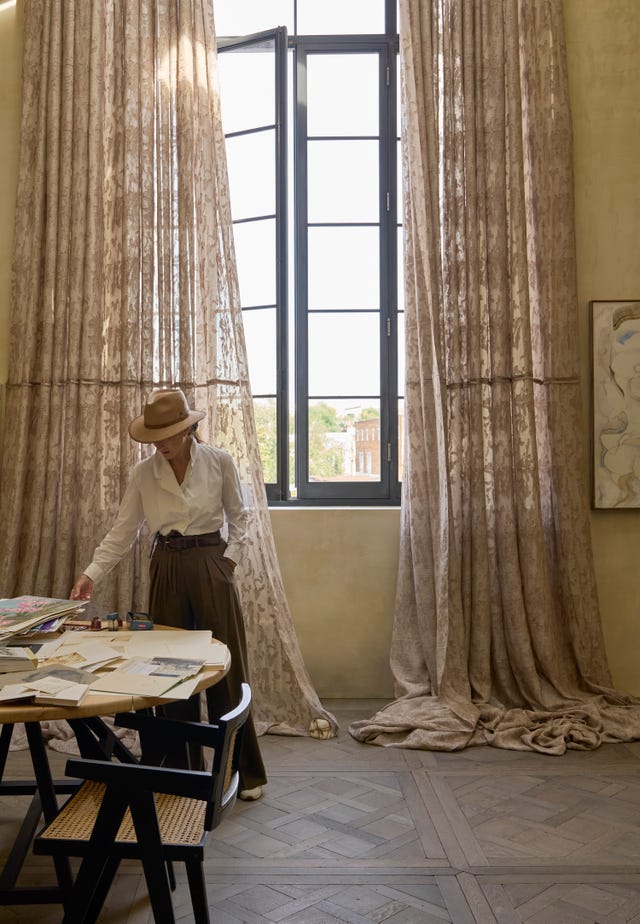 a woman standing in front of a large window dressed with curtains