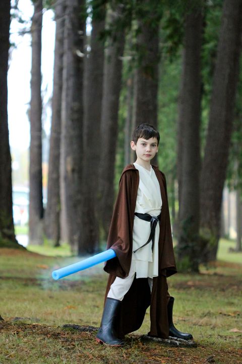 boy standing outside dressed as obi wan with blue pool noodle as light saber and long brown robe