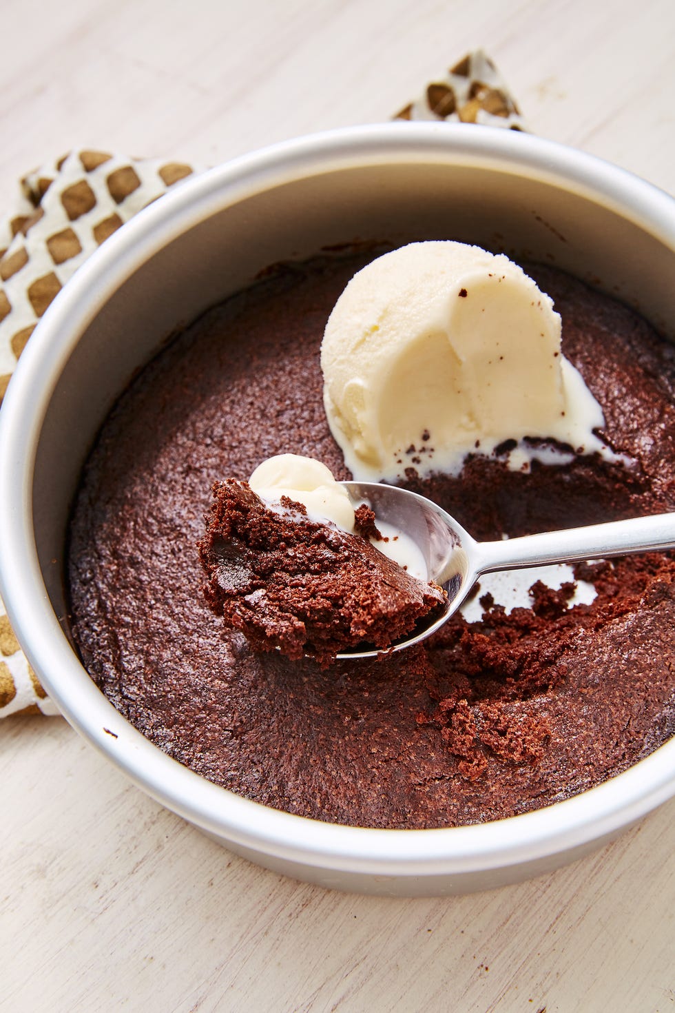 air fryer brownie in a small circular pan with vanilla ice cream and a spoon