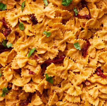 a pot of bowtie pasta in a creamy sauce with pieces of sun dried tomato, chopped basil, and parmesan cheese