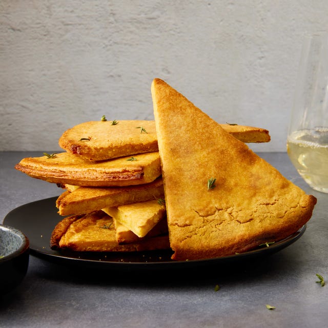 a golden brown mediterranean chickpea flatbread in a cast iron skillet with crispy edges and fresh herbs sprinkled on top