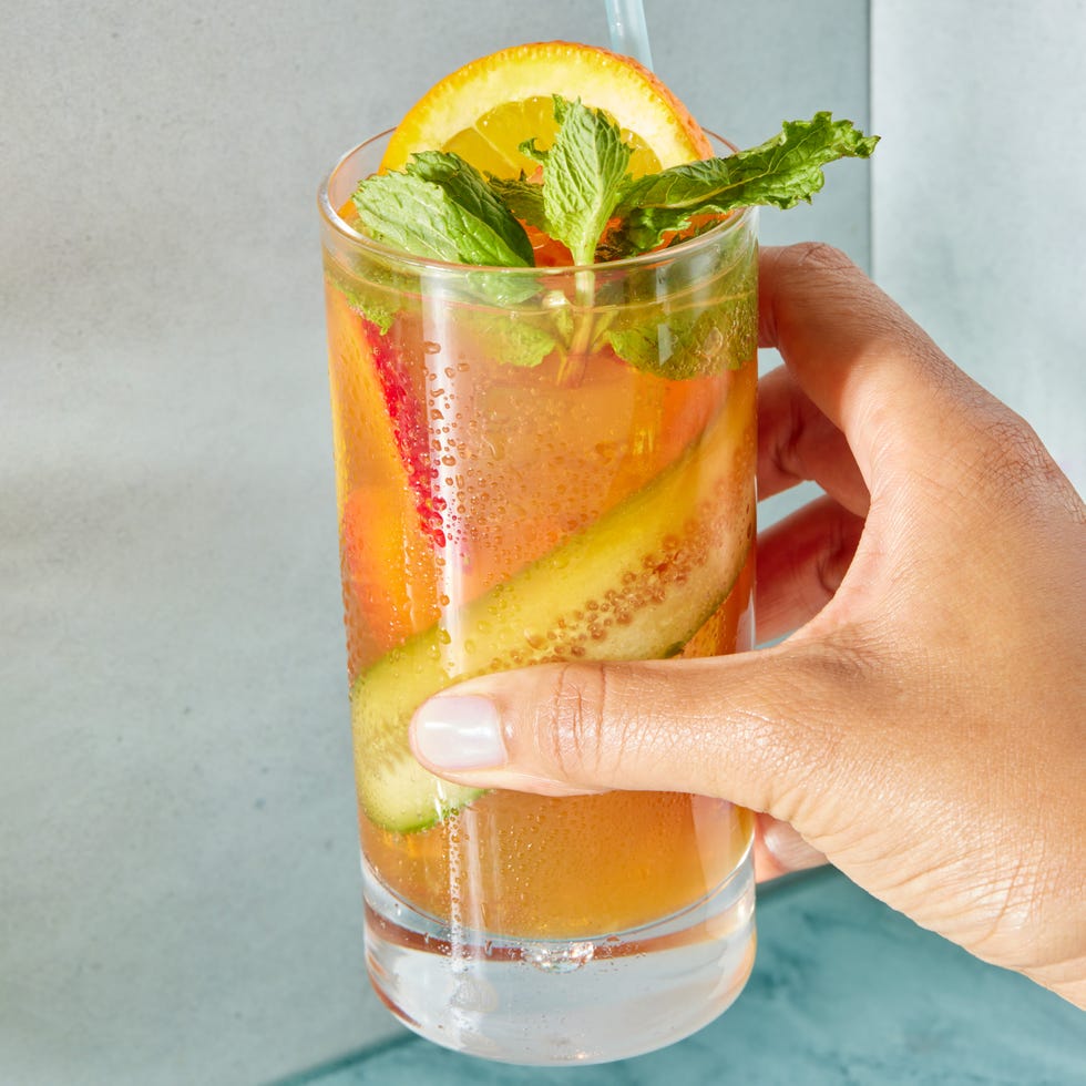 two tall cocktail glasses garnished with a cucumber slice, strawberries, orange, lemon, and mint and filled with ginger ale and pimm's no 1