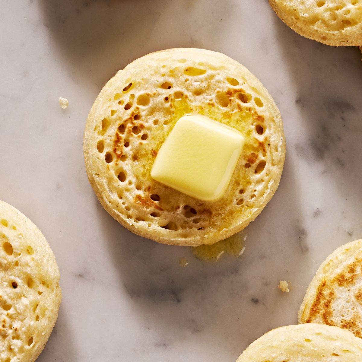 crumpet topped with butter surrounded by more crumpets