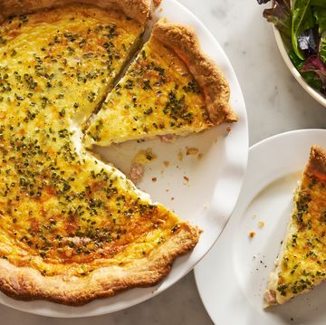 ham and cheese quiche with a slice on a plate beside it and a salad bowl nearby