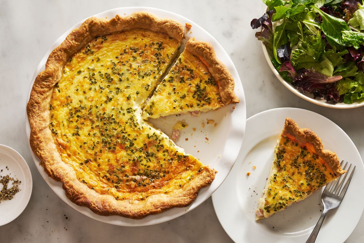 ham and cheese quiche beside a plate with a slice of quiche and a salad bowl