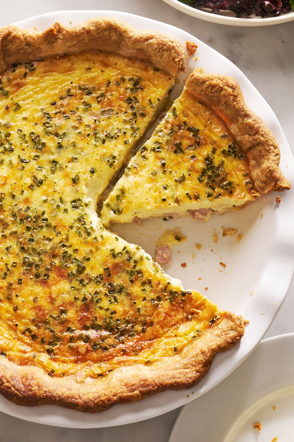 ham and cheese quiche with a slice cut out beside a salad bowl