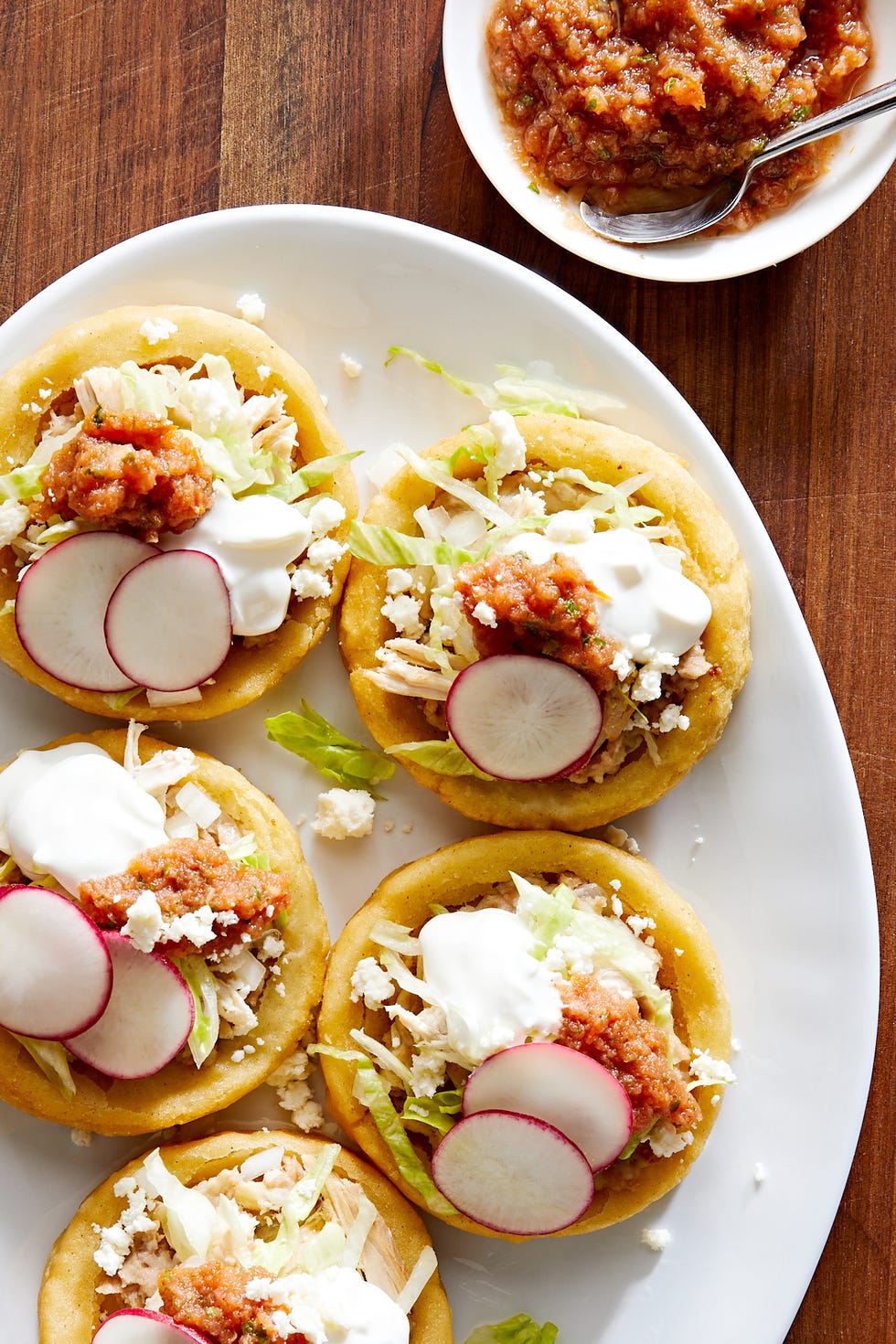 sopes made of masa harina and topped with refried beans salsa roja shredded lettuce mexican crema radishes and cojita