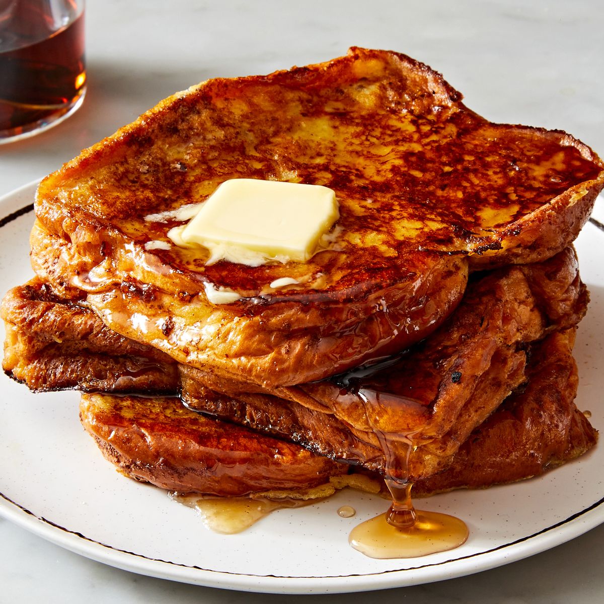 a stack of french toast on a white plate with butter and maple syrup