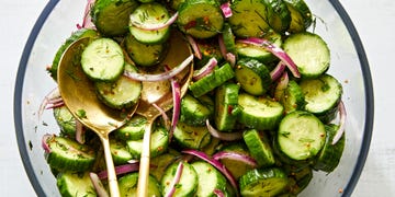 a salad bowl filled with sliced cucumber rounds and thinly sliced raw red onion tossed in a dressing made with whole mustard seeds and chopped fresh dill and chives