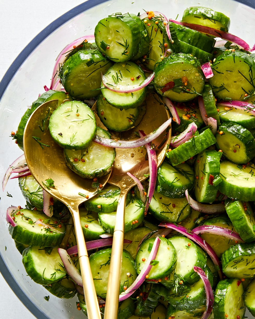 a salad bowl filled with sliced cucumber rounds and thinly sliced raw red onion tossed in a dressing made with whole mustard seeds and chopped fresh dill and chives