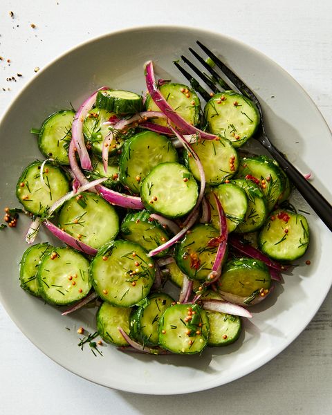 a salad bowl filled with sliced cucumber rounds and thinly sliced raw red onion tossed in a dressing made with whole mustard seeds and chopped fresh dill and chives