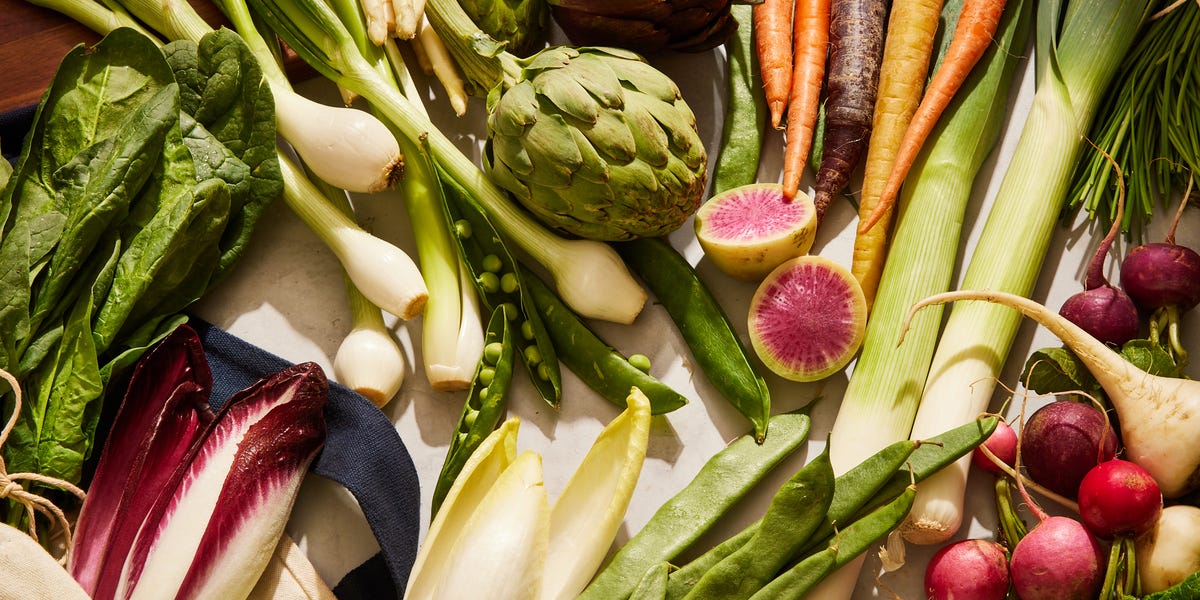 leeks, endive, artichokes, radishes, fava beans, peas, spinach, and carrots arranged on a marble surface
