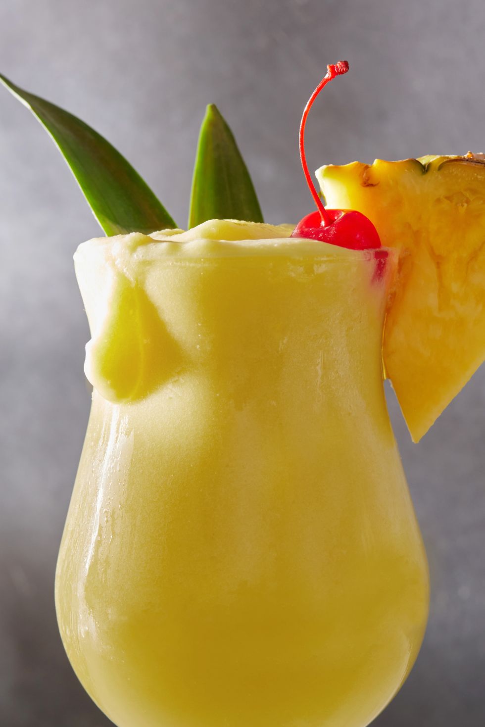 frozen pina colada cocktail with dark rum garnished with a maraschino cherry and pineapple wedge