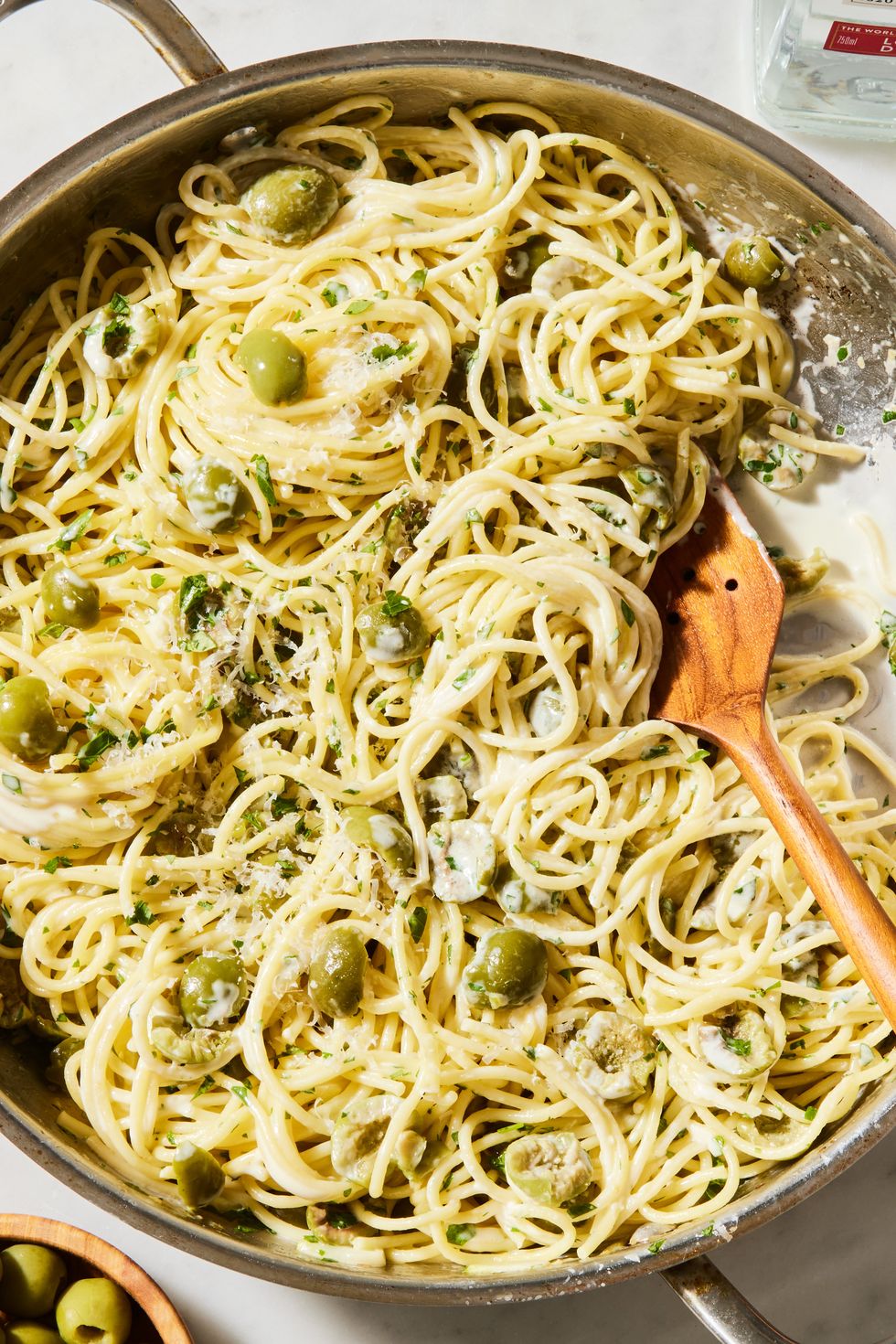 a pot of cooked spaghetti in a cream sauce with pieces of green olives, chopped parsley, and parmesan