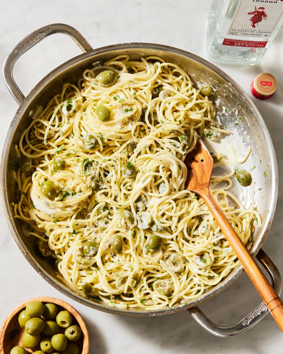 a pot of cooked spaghetti in a cream sauce with pieces of green olive, chopped parsley, and parmesan