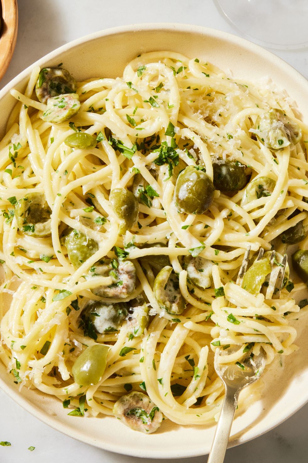 a pot of cooked spaghetti in a cream sauce with pieces of green olive, chopped parsley, and parmesan