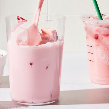 a tall glass filled with a creamy light pink beverage, ice, and sliced fresh strawberries