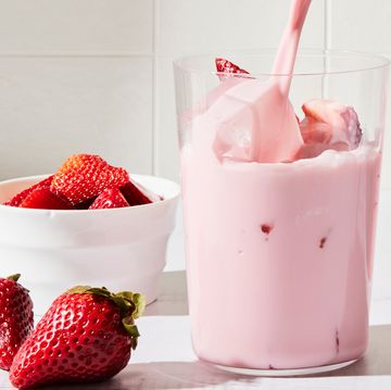 a tall glass filled with a creamy light pink beverage, ice, and sliced fresh strawberries