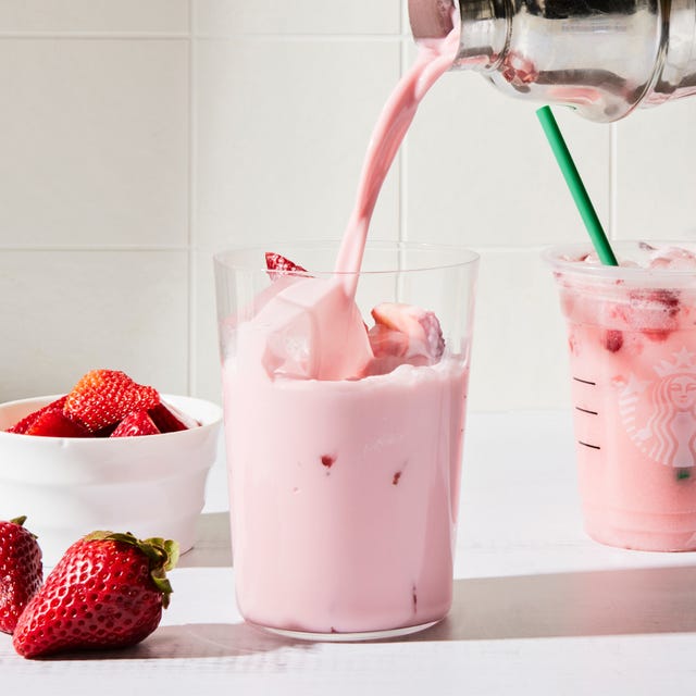 a tall glass filled with a creamy light pink beverage, ice, and sliced fresh strawberries