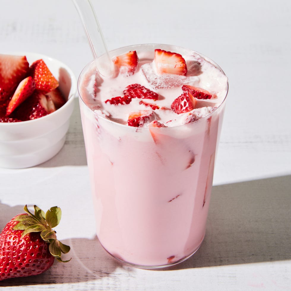 a tall glass filled with a creamy light pink beverage, ice, and sliced fresh strawberries