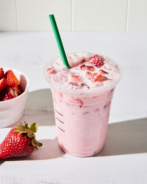 a tall glass with creamy light pink beverage on ice with sliced fresh strawberries and a glass straw