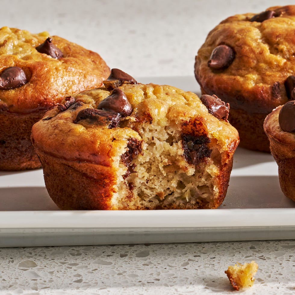 a batch of golden brown banana muffins with chocolate chips on a white surface