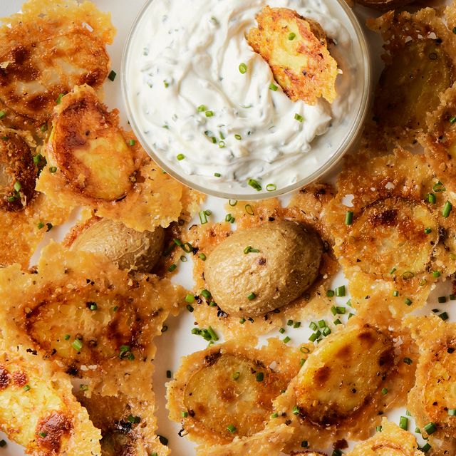 crispy parmesan potatoes on a sheet tray with a bowl of sour cream and chive dip