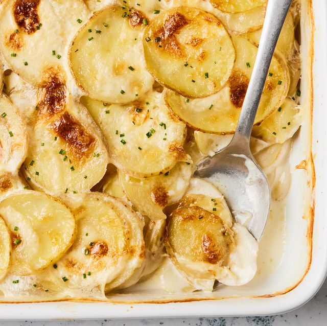 scalloped potatoes in a white baking dish with a silver serving spoon