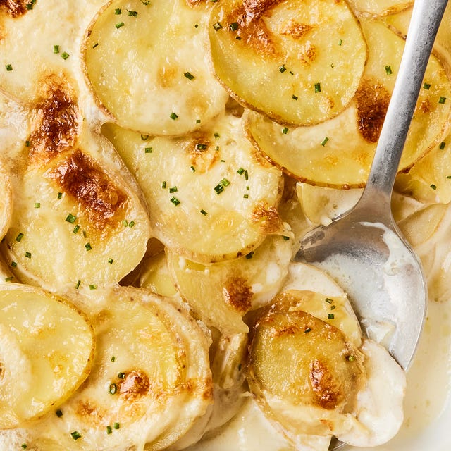 scalloped potatoes in a white baking dish with a silver serving spoon